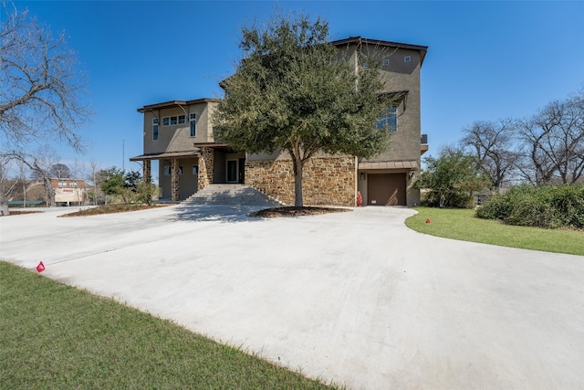 view of front of house with concrete driveway, a front yard, stucco siding, stone siding, and an attached garage