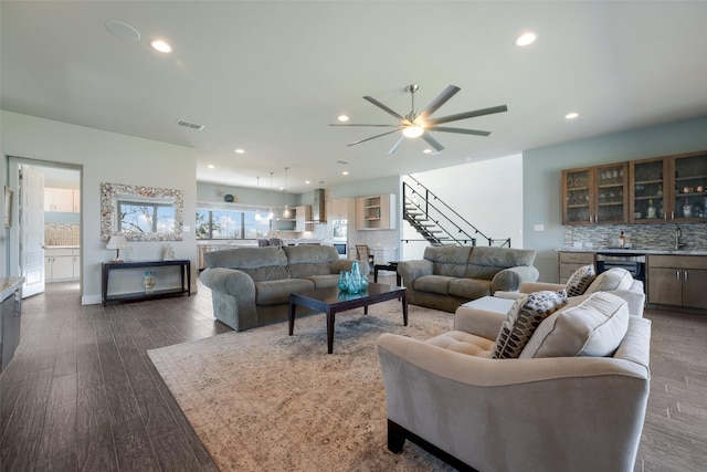 living room with dark wood-style floors, recessed lighting, wet bar, ceiling fan, and stairs