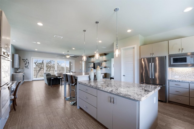 kitchen with built in microwave, stainless steel refrigerator, dark wood-style flooring, and decorative backsplash