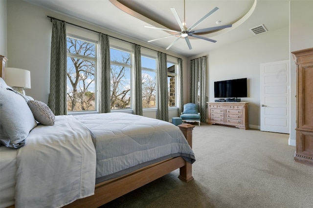 bedroom featuring visible vents, baseboards, ceiling fan, a tray ceiling, and carpet flooring