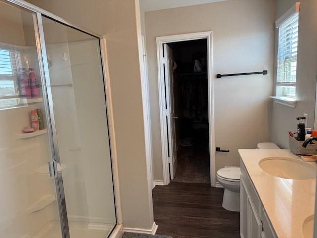 full bathroom featuring a walk in closet, toilet, a stall shower, wood finished floors, and vanity