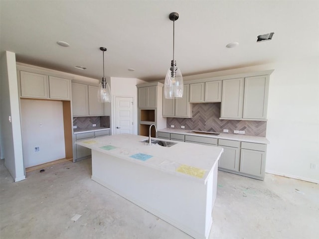 kitchen with a sink, backsplash, a kitchen island with sink, and unfinished concrete floors