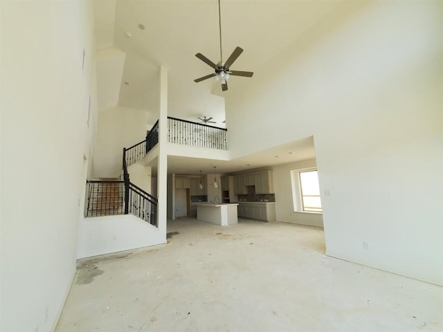 unfurnished living room featuring a ceiling fan, unfinished concrete floors, a towering ceiling, and stairs