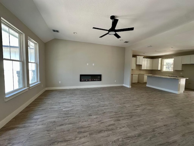 unfurnished living room with dark wood-type flooring, baseboards, a glass covered fireplace, and lofted ceiling