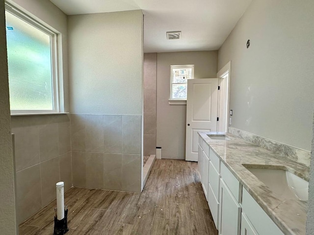 full bathroom with double vanity, visible vents, a tile shower, wood finished floors, and a sink