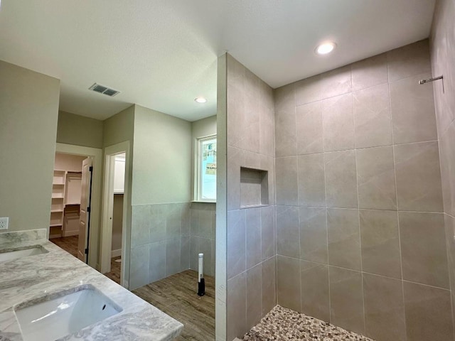 bathroom featuring a walk in closet, visible vents, tile walls, a sink, and tiled shower