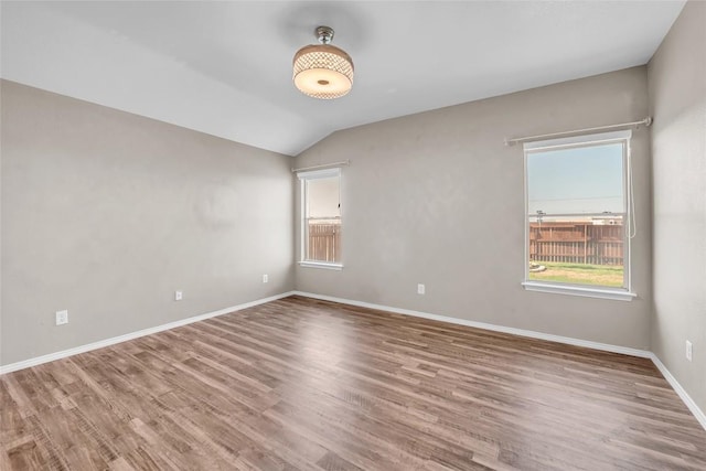 spare room with a healthy amount of sunlight, baseboards, lofted ceiling, and wood finished floors