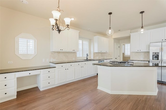 kitchen with a sink, stainless steel appliances, white cabinetry, dark countertops, and light wood-type flooring