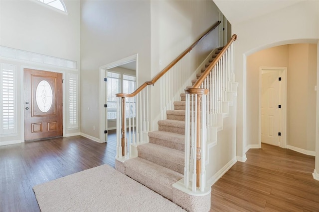entrance foyer with arched walkways, stairs, baseboards, wood finished floors, and a towering ceiling