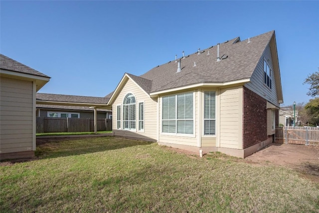 rear view of house with a yard, fence, and a shingled roof