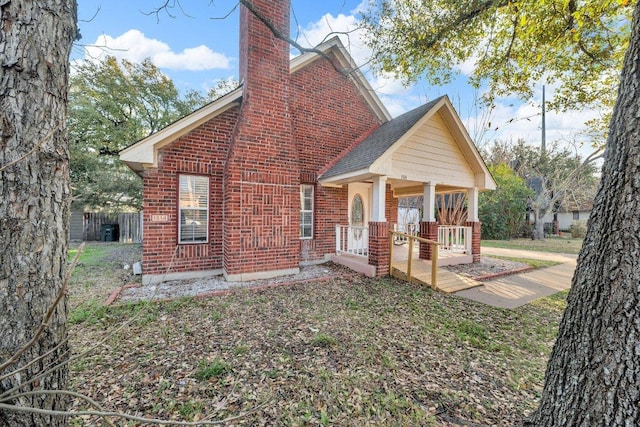 rear view of house with a chimney, covered porch, and brick siding