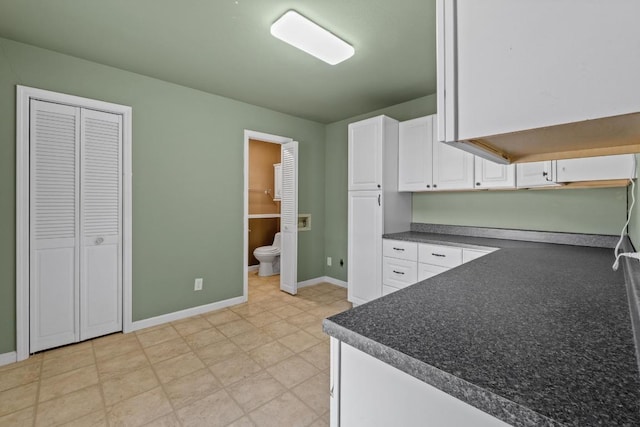 kitchen with baseboards, dark countertops, and white cabinetry