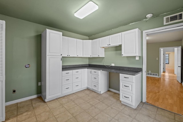 kitchen featuring white cabinetry, dark countertops, visible vents, and built in study area