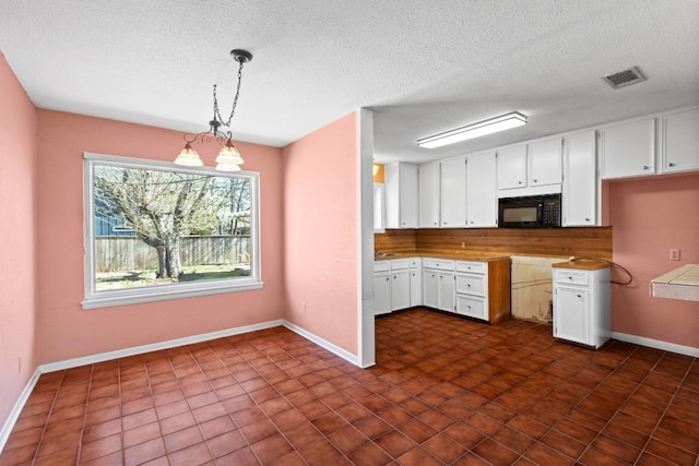 kitchen featuring hanging light fixtures, white cabinets, visible vents, and black microwave