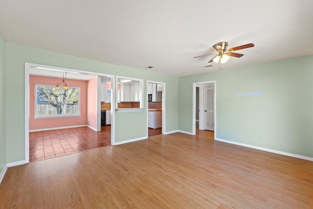 unfurnished living room featuring visible vents, ceiling fan with notable chandelier, light wood-type flooring, and baseboards