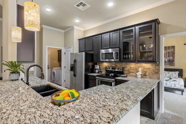 10033 Longhorn Skwy, Dripping Springs, TX 78620 - kitchen featuring appliances with stainless steel finishes, washer / dryer, a sink, light stone counters, and ornamental molding