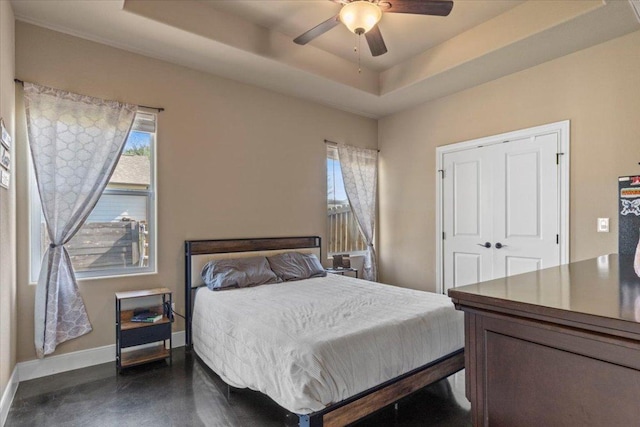 bedroom featuring multiple windows, baseboards, a tray ceiling, and a ceiling fan