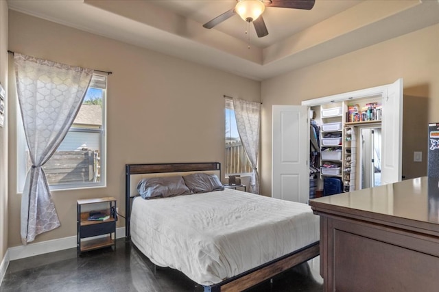 bedroom featuring a walk in closet, multiple windows, a raised ceiling, and baseboards