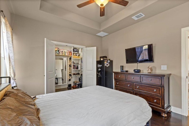 bedroom with visible vents, dark wood-type flooring, freestanding refrigerator, baseboards, and a raised ceiling