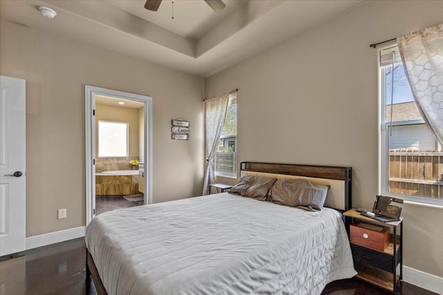 bedroom featuring ceiling fan, baseboards, a raised ceiling, and ensuite bath