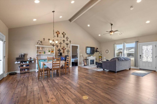 dining space with visible vents, beam ceiling, ceiling fan with notable chandelier, a glass covered fireplace, and dark wood-style floors