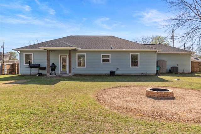 rear view of house featuring central AC unit, fence, roof with shingles, an outdoor fire pit, and a yard