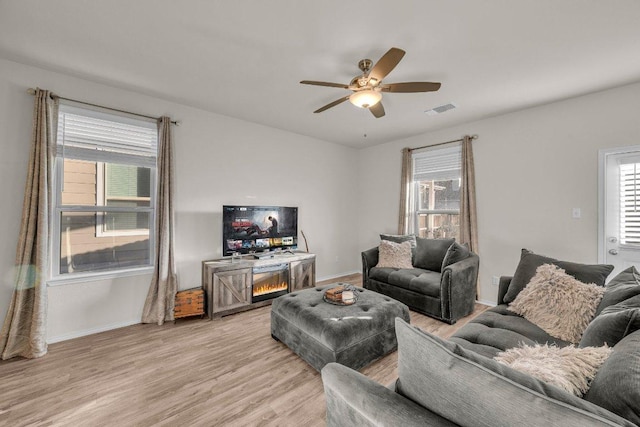 living area with baseboards, visible vents, light wood finished floors, and ceiling fan