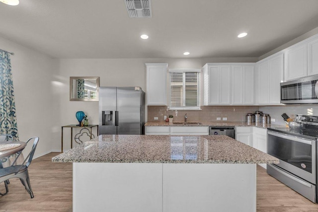 kitchen with a sink, stainless steel appliances, light wood-type flooring, backsplash, and a center island