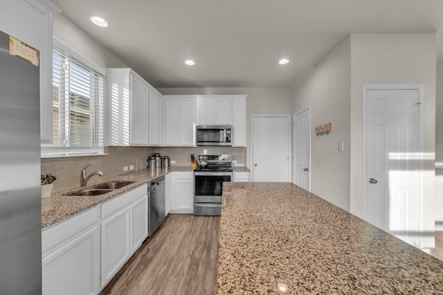 kitchen featuring light wood-style flooring, a sink, appliances with stainless steel finishes, white cabinets, and decorative backsplash