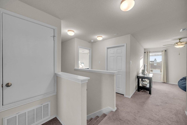 corridor featuring an upstairs landing, visible vents, a textured ceiling, and light carpet