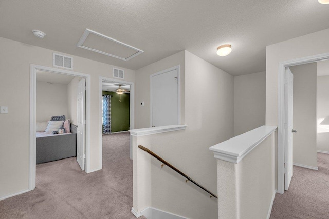 corridor with visible vents, an upstairs landing, a textured ceiling, and carpet floors