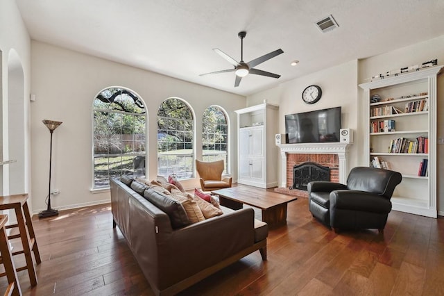 living room with visible vents, dark wood-type flooring, baseboards, ceiling fan, and a fireplace