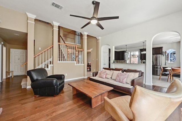 living area featuring visible vents, wood finished floors, arched walkways, ceiling fan, and stairs