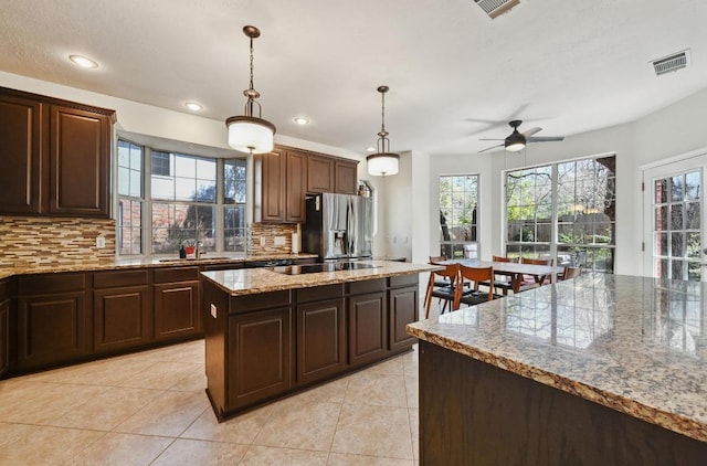 kitchen with a sink, stainless steel refrigerator with ice dispenser, black electric stovetop, backsplash, and a center island