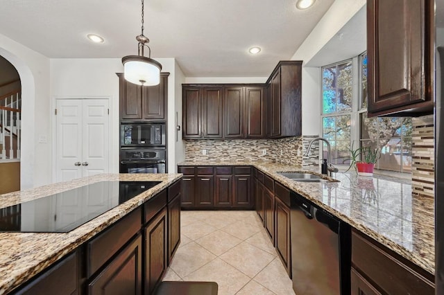 kitchen with light stone countertops, arched walkways, a sink, black appliances, and dark brown cabinetry