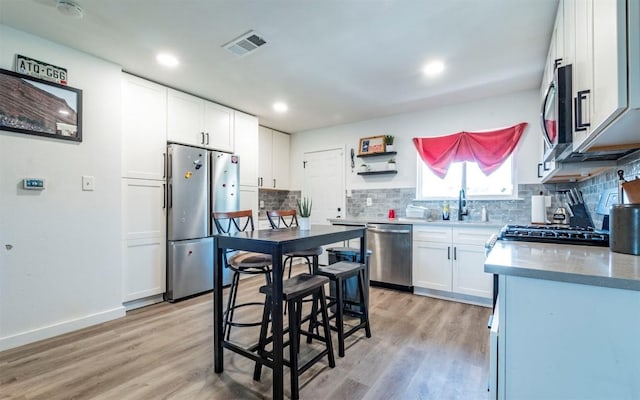 kitchen featuring tasteful backsplash, visible vents, light wood-style floors, stainless steel appliances, and a sink