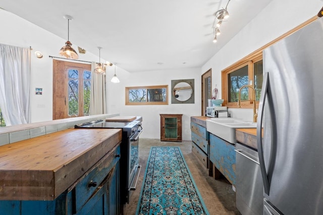 kitchen with pendant lighting, a sink, wood counters, stainless steel appliances, and concrete flooring