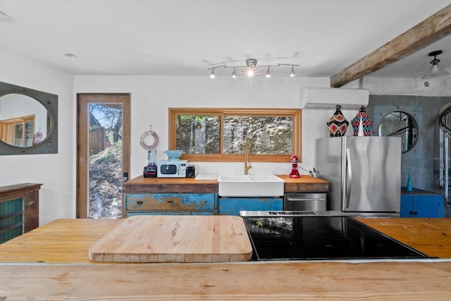 kitchen with a wall unit AC, freestanding refrigerator, a sink, rail lighting, and beamed ceiling