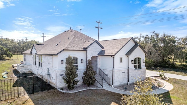 view of front of house with fence, stone siding, roof with shingles, and stucco siding