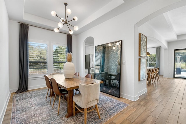 dining area featuring an inviting chandelier, a raised ceiling, light wood-style floors, and arched walkways