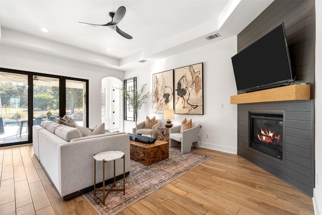 living area featuring visible vents, a fireplace, light wood finished floors, baseboards, and ceiling fan