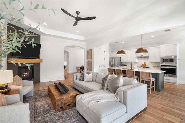 living area with visible vents, a ceiling fan, a tray ceiling, arched walkways, and light wood finished floors