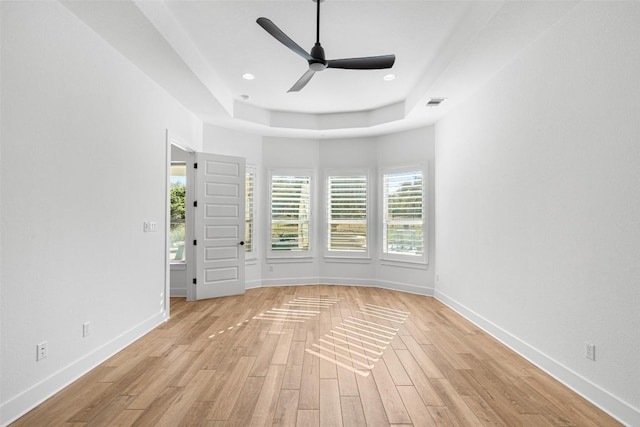 empty room with ceiling fan, baseboards, light wood-type flooring, a tray ceiling, and recessed lighting