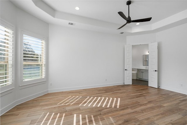 unfurnished bedroom featuring light wood finished floors, visible vents, baseboards, a tray ceiling, and recessed lighting