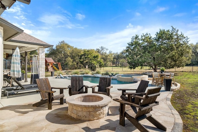 view of patio / terrace with a playground, fence, a pool with connected hot tub, and a fire pit