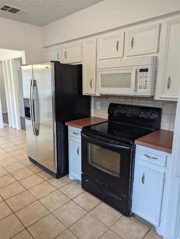 kitchen featuring electric range, visible vents, dark countertops, stainless steel fridge, and white microwave