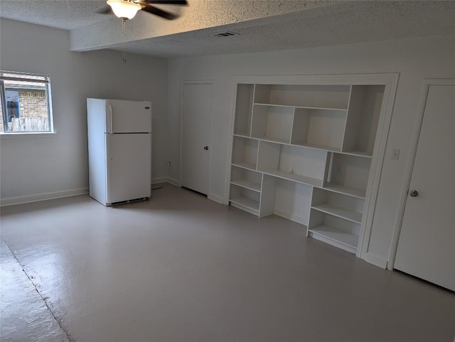 interior space featuring visible vents, a textured ceiling, freestanding refrigerator, and finished concrete flooring