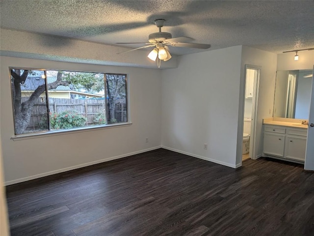 unfurnished bedroom featuring a ceiling fan, baseboards, dark wood-type flooring, ensuite bathroom, and a textured ceiling