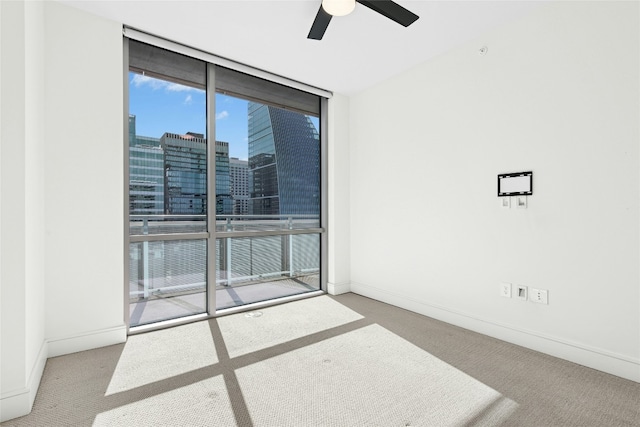 spare room with a city view, floor to ceiling windows, a ceiling fan, and carpet floors