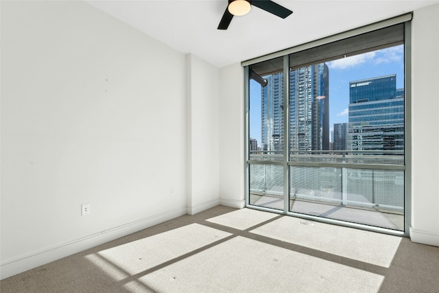 unfurnished room with a ceiling fan, baseboards, floor to ceiling windows, a view of city, and carpet flooring